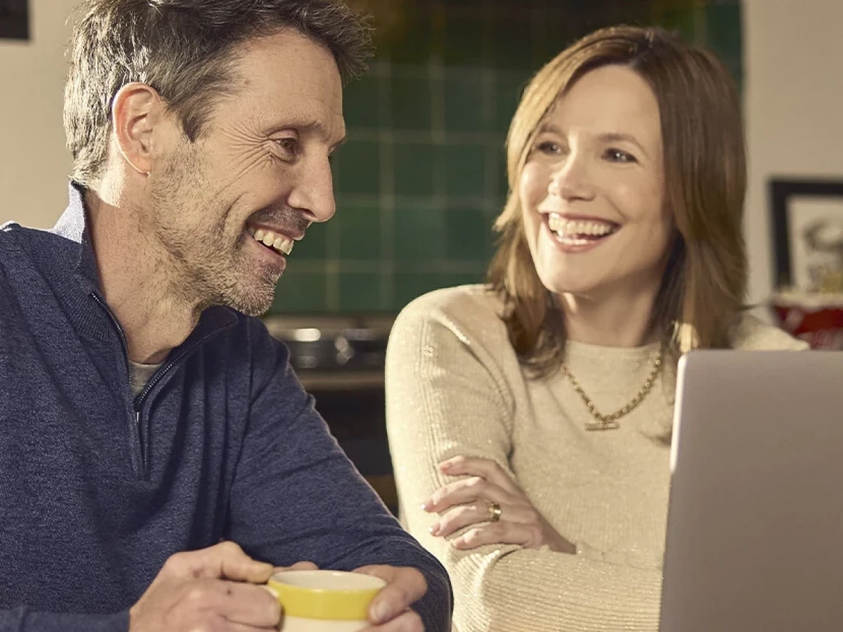 Two adults smiling beside a laptop at a kitchen table, with a mug of tea, in County Durham.