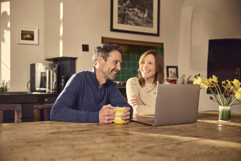 Happy couple smiling at the laptop with streaming internet.