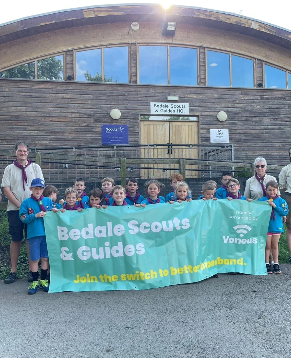 Bedale Scouts and Guides members with a Voneus broadband banner outside their headquarters, celebrating their community broadband connection in Bedale,