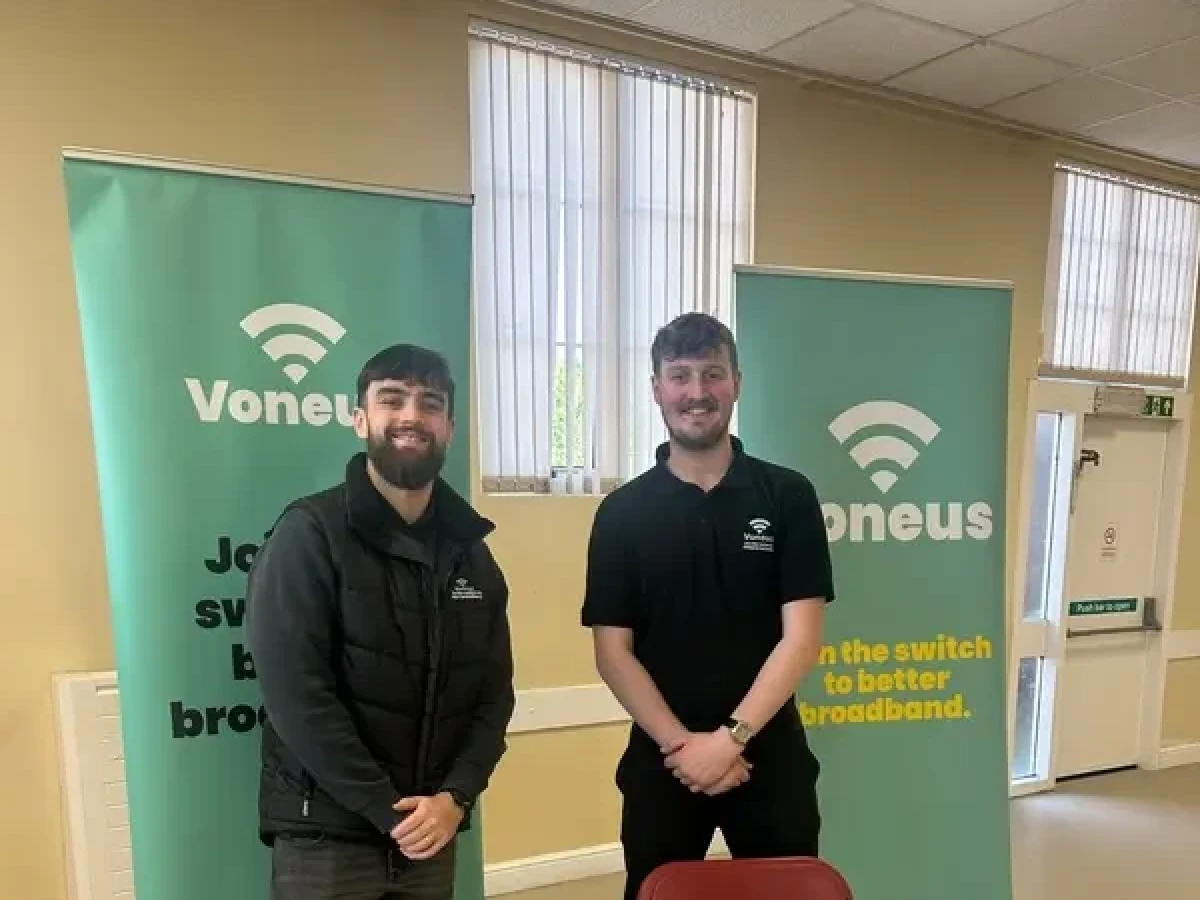 Two Voneus team members standing beside broadband banners and information leaflets in a community hall in County Durham.